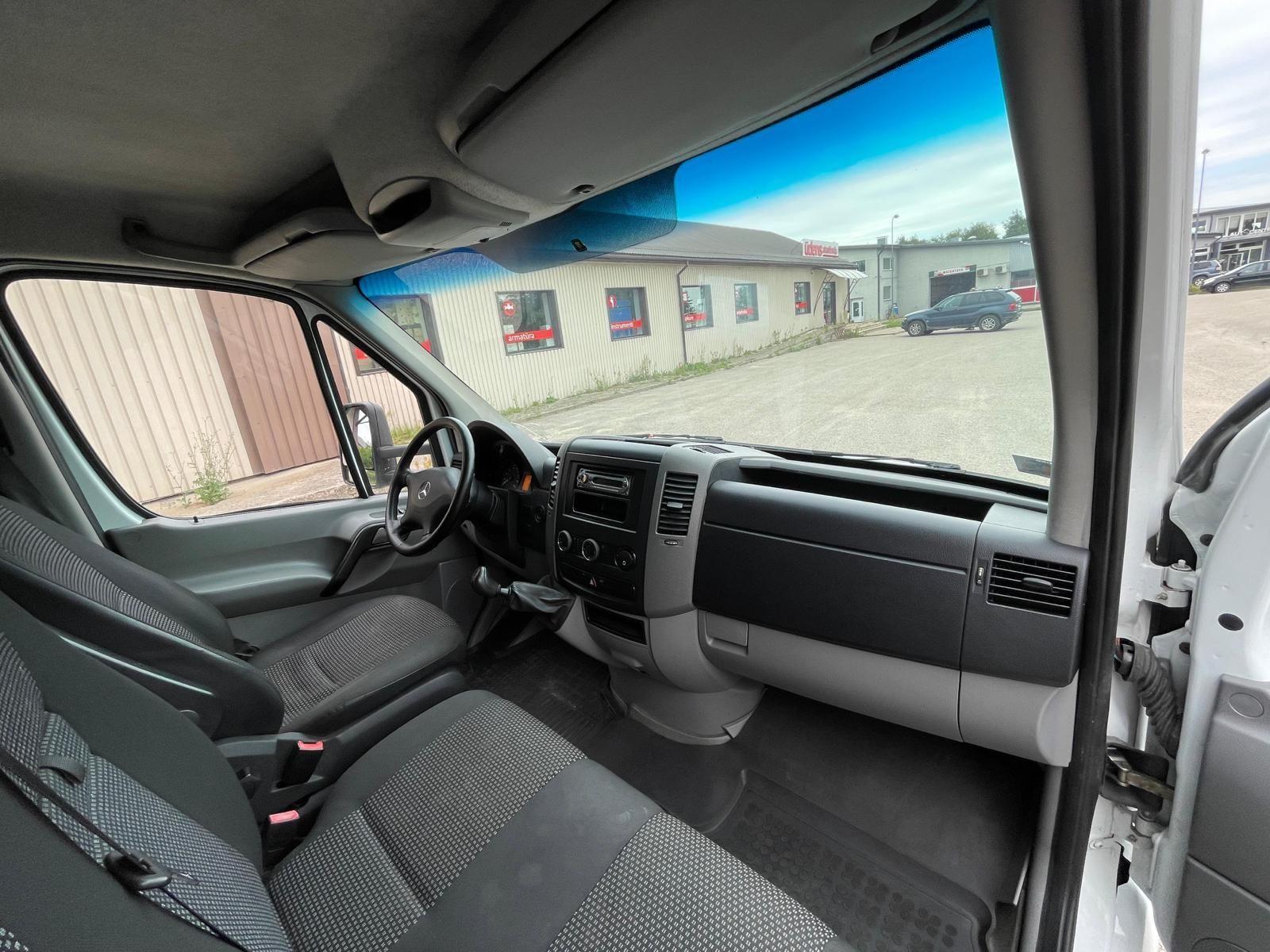 Balta furgona interjers ar melniem sēdekļiem un stūri.