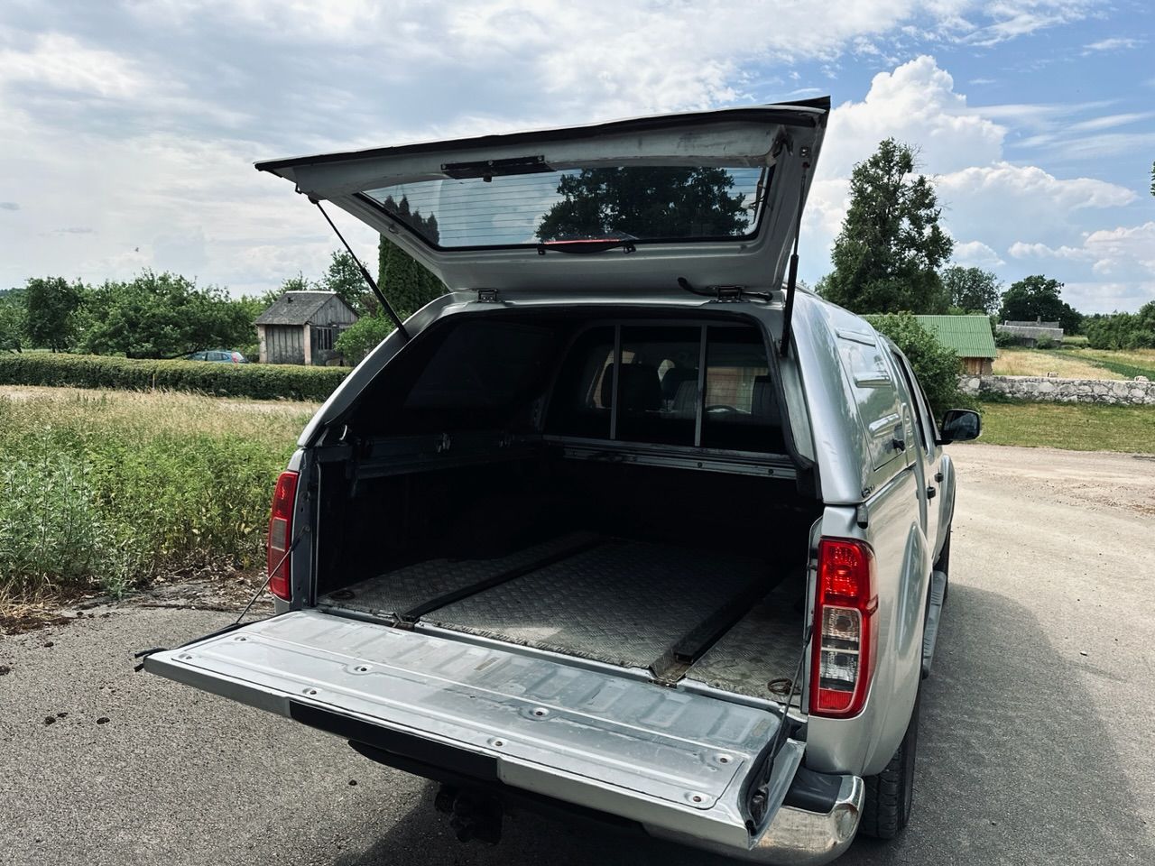 Sudraba kravas automašīnas aizmugure ar atvērtu bagāžnieku