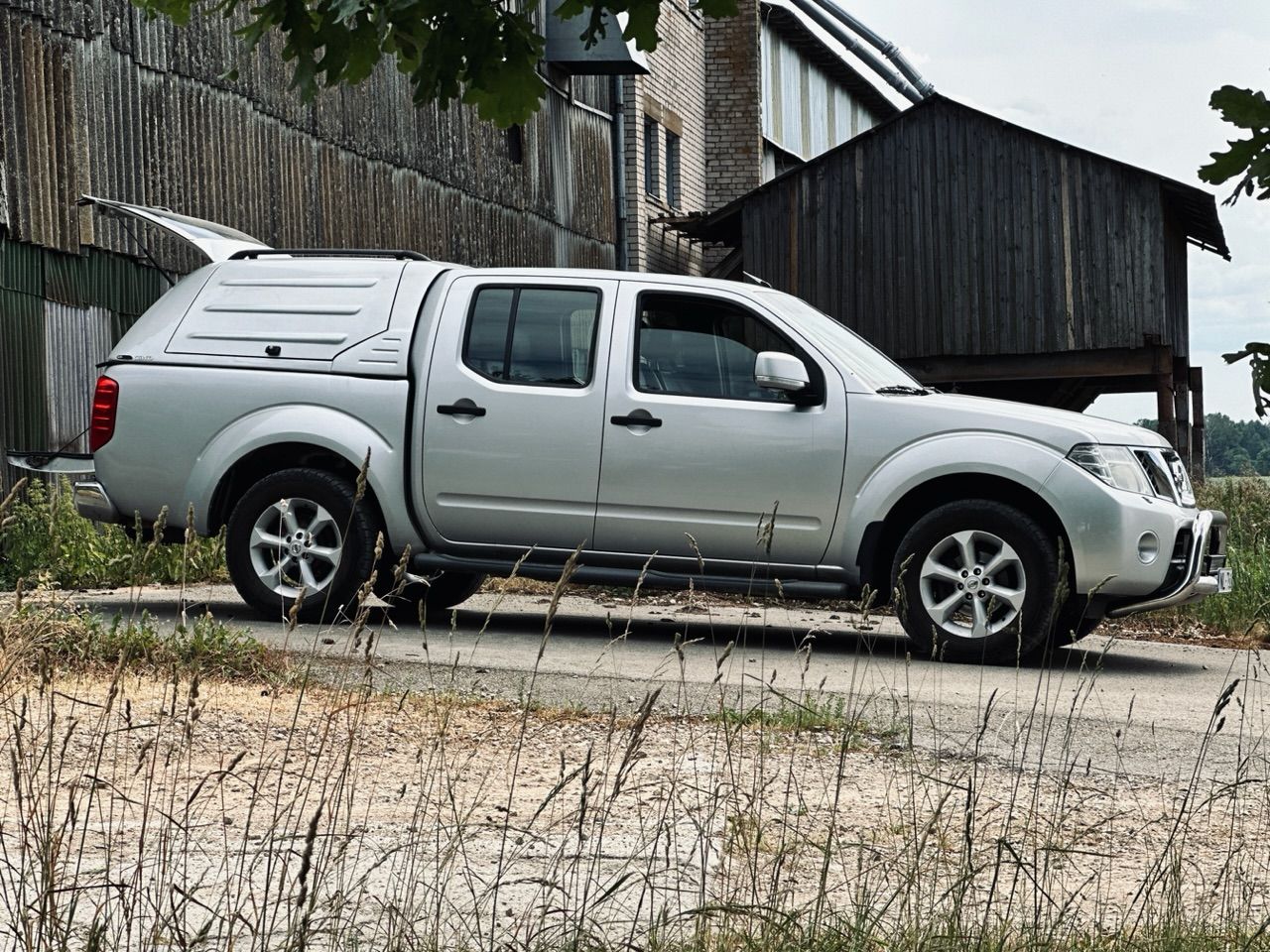 Ceļa malā stāv sudraba kravas automašīna ar nojumi.