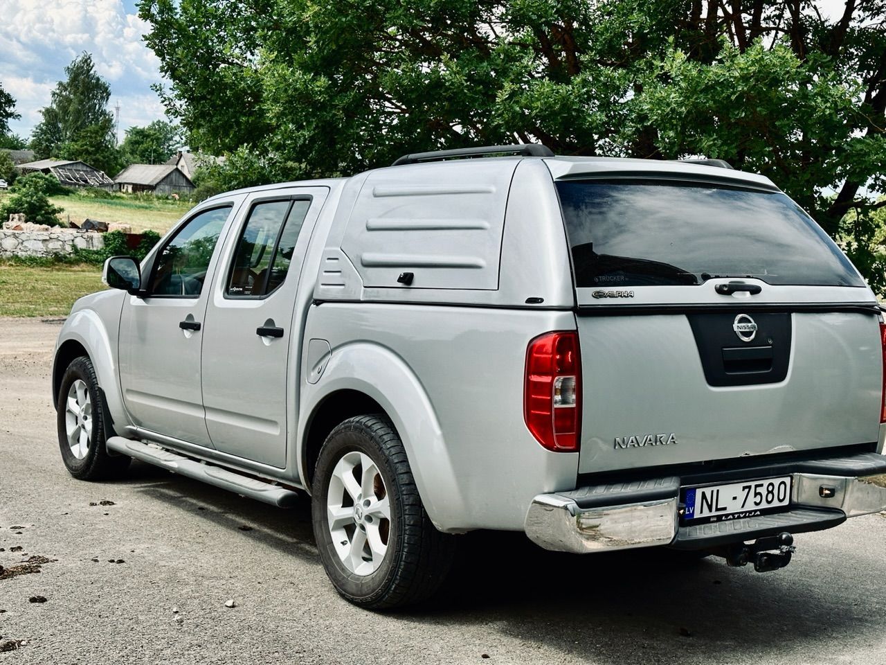 Ceļa malā stāv sudraba krāsas pikaps nissan ar nojumi.