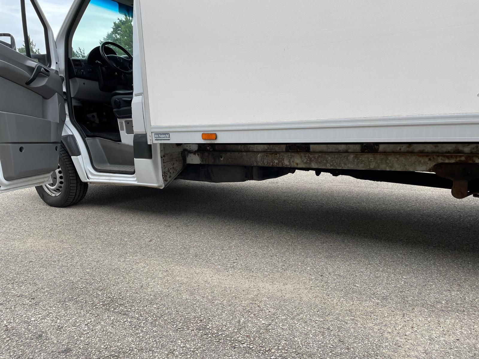 Ceļa malā stāv balts furgons ar atvērtām durvīm.