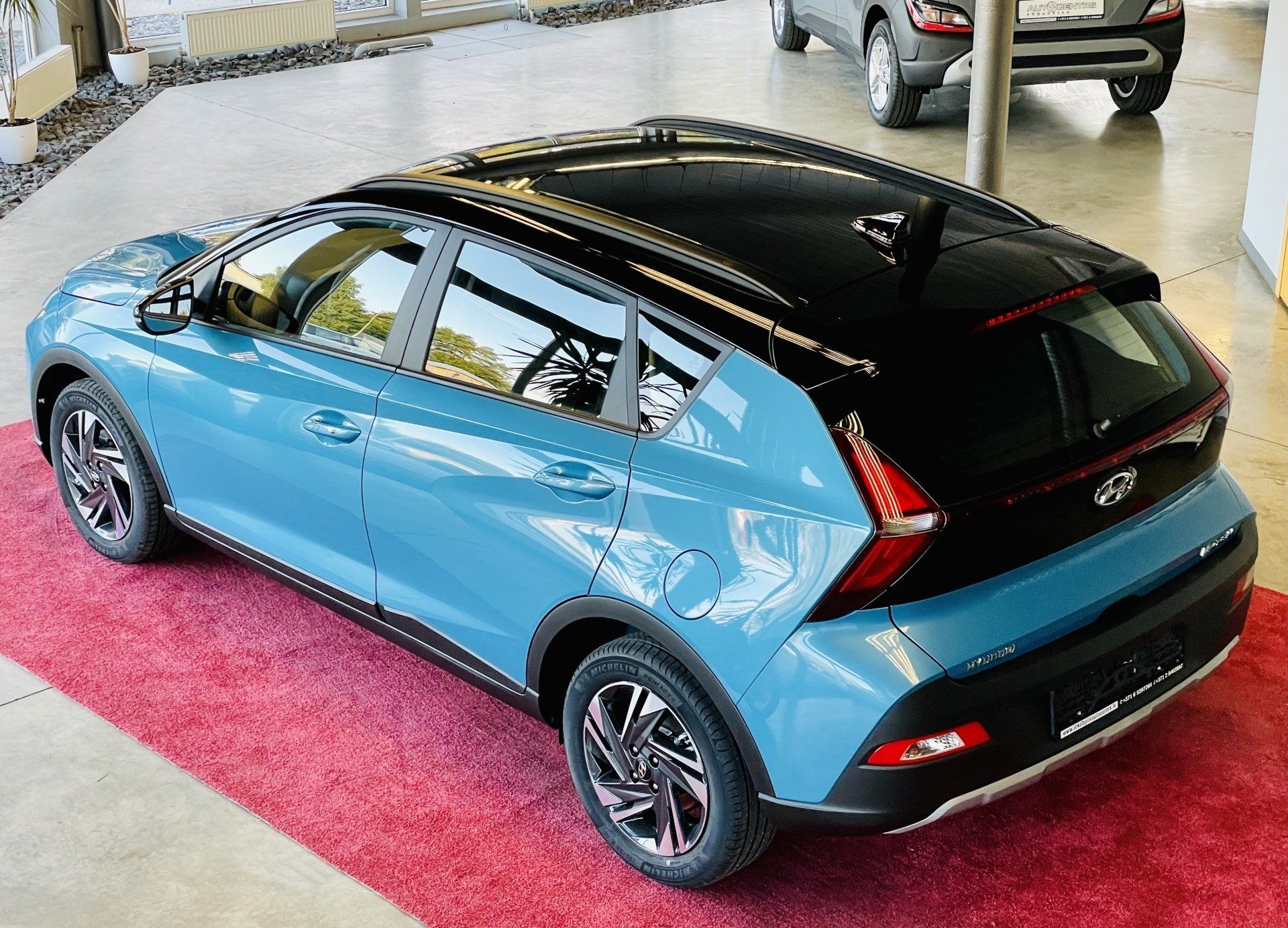 Autosalonā ir izstādīta zila mašīna ar melnu jumtu.