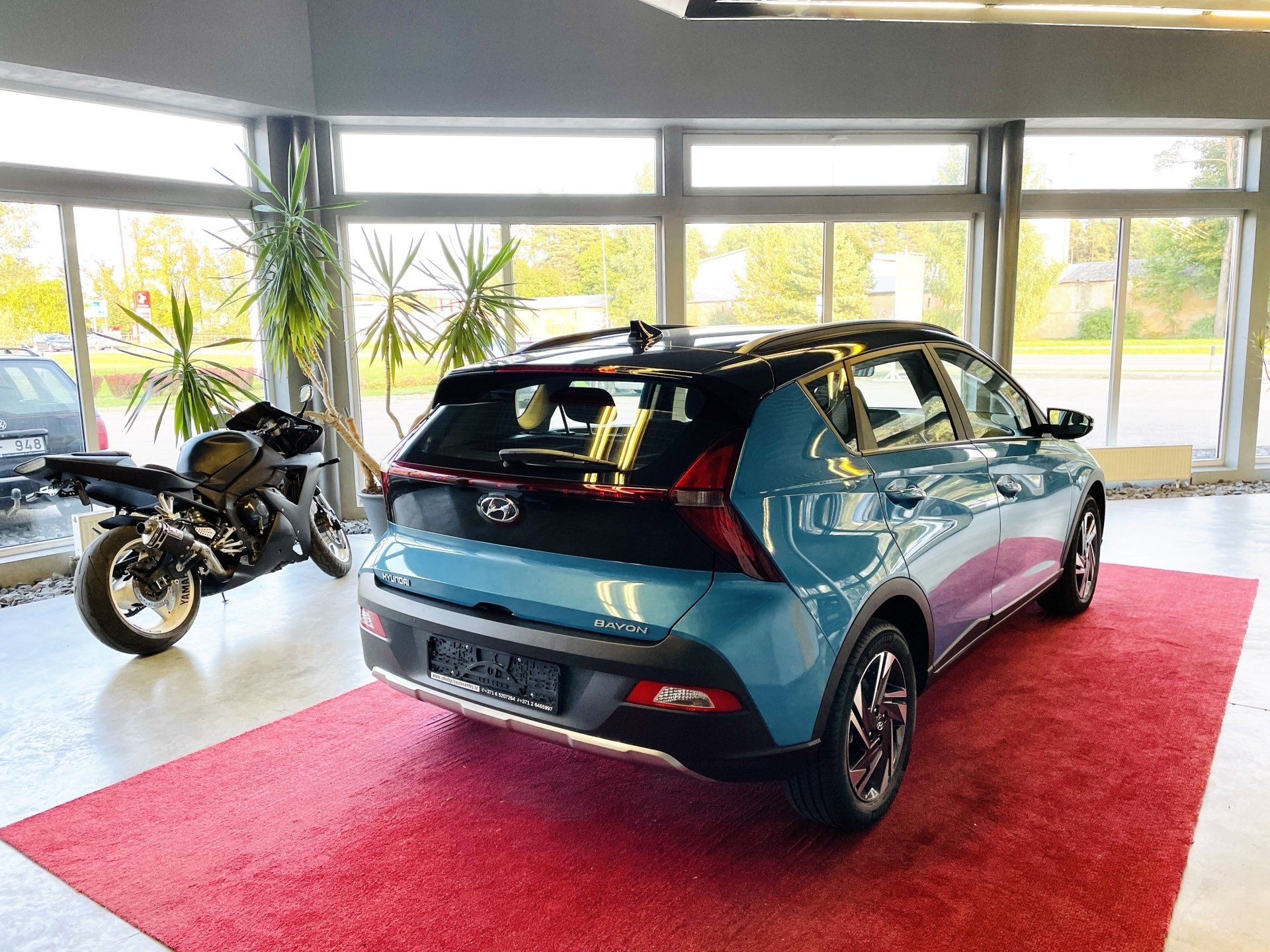 Zila automašīna ir novietota salonā pie motocikla.