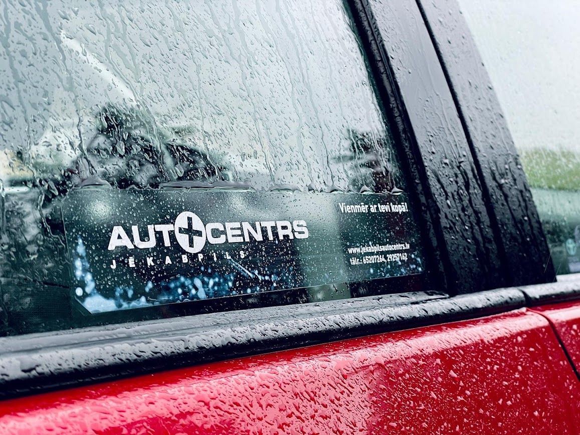 Sarkana mašīna ar uzlīmi uz loga rakstīts autocentrs.