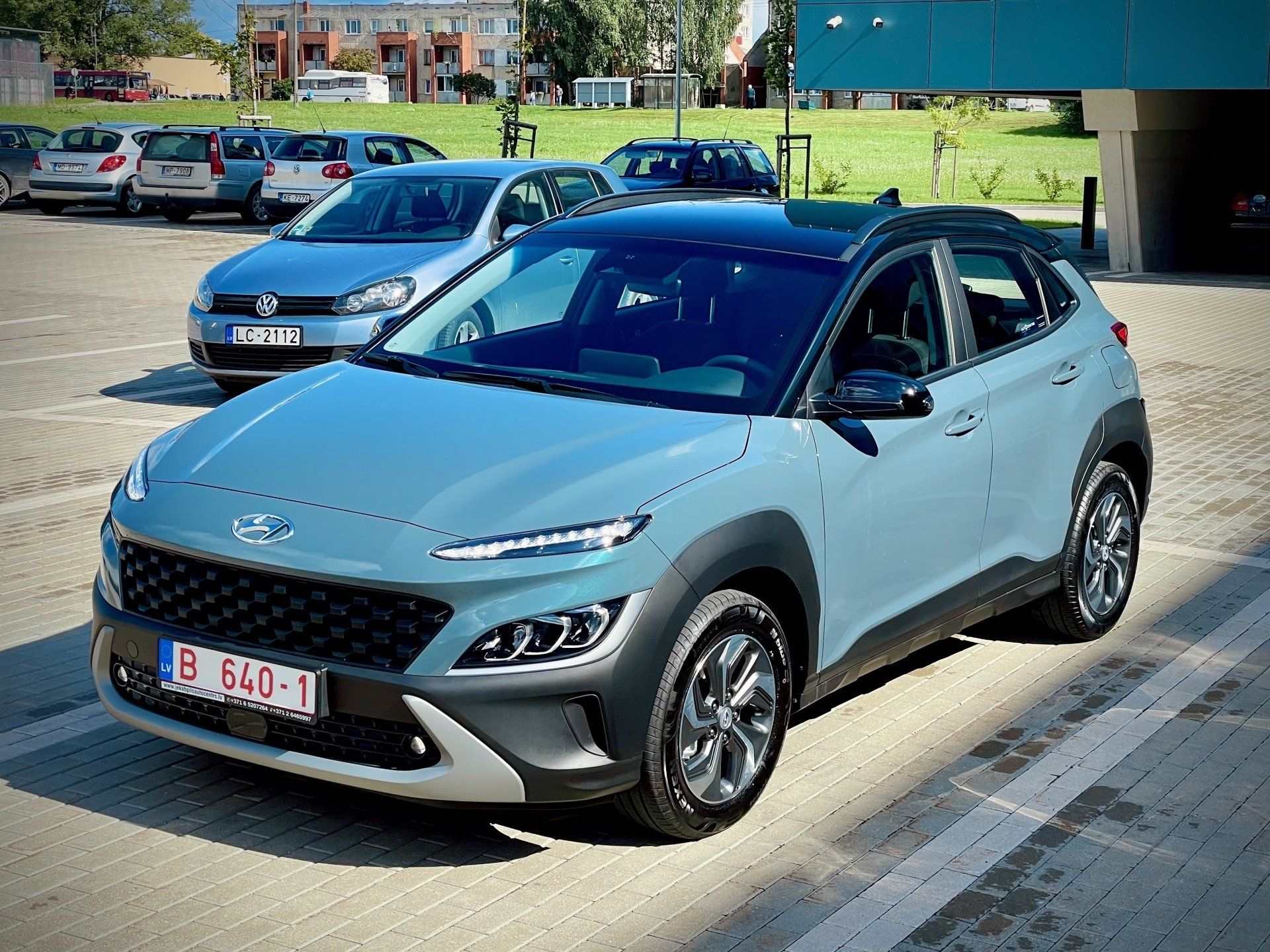 Autostāvvietā blakus citām automašīnām ir novietota zila automašīna.