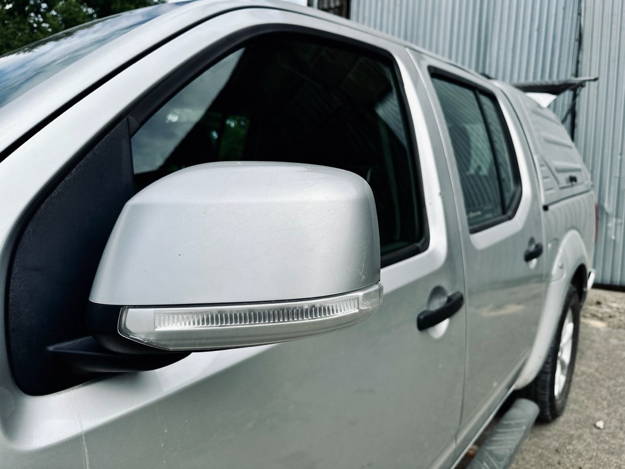 Sudraba kravas automašīna ar nojume ir novietota pie ēkas.