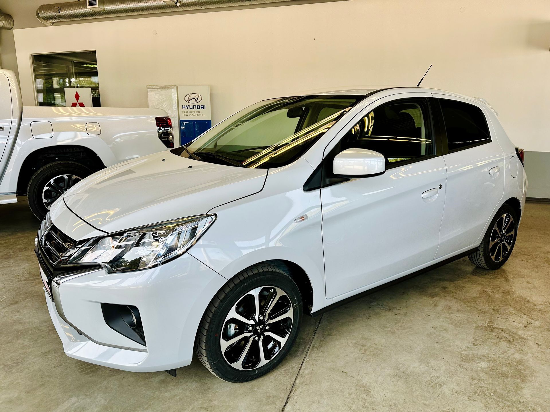 Balta automašīna ir novietota garāžā blakus kravas automašīnai.