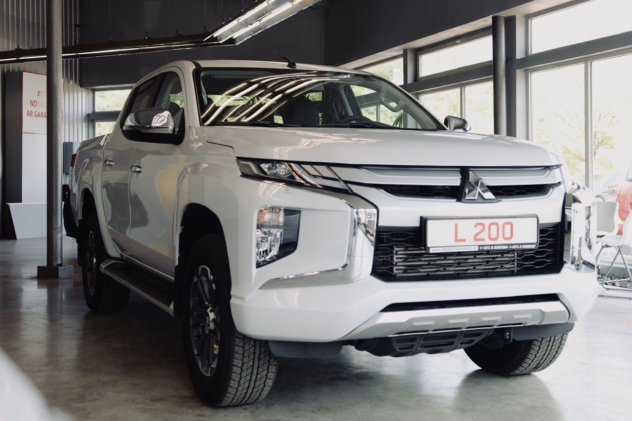 Balts mitsubishi l200 pikaps ir novietots izstāžu zālē.