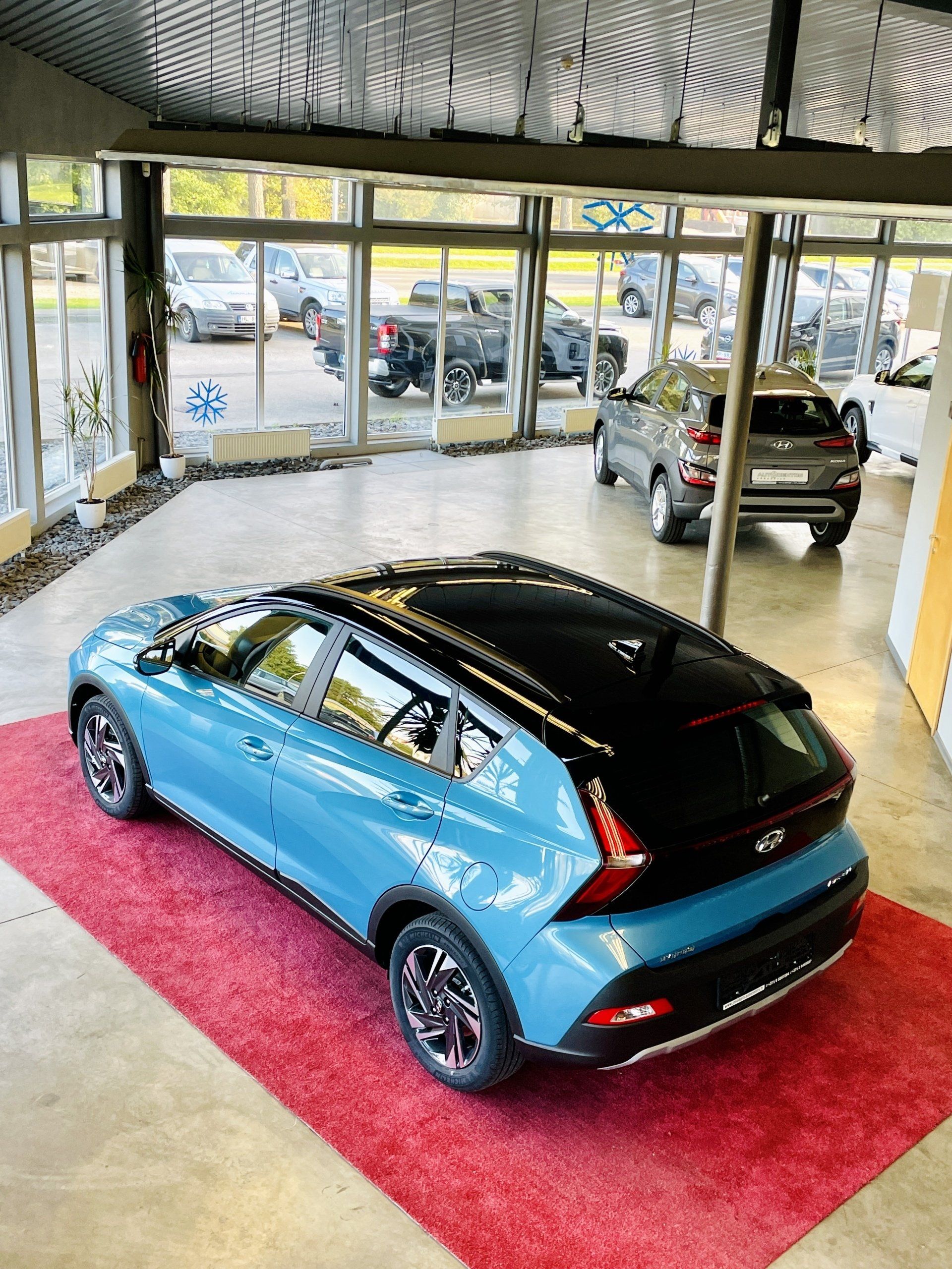 Izstāžu zālē uz sarkana paklāja sēž zila mašīna.