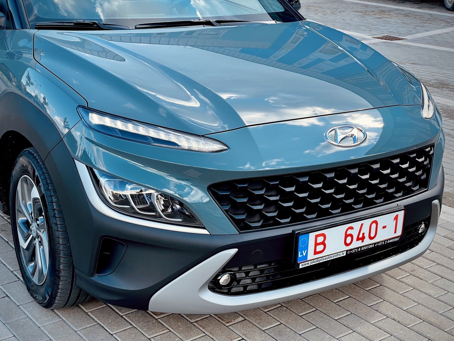 Zila automašīna ar numura zīmi, kurā rakstīts b 640-1, ir novietota uz ķieģeļu ietves.