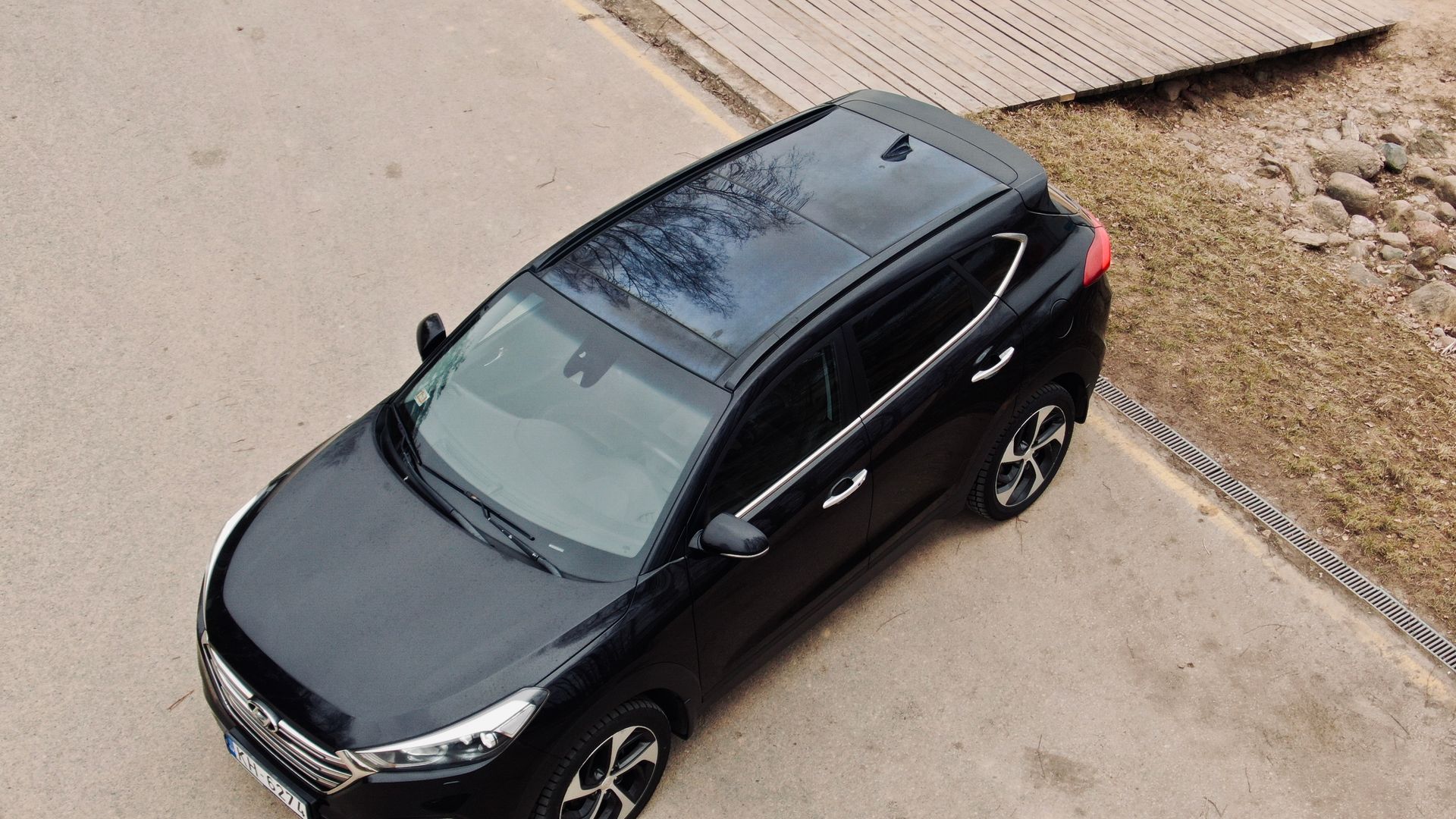 Skats no gaisa uz ceļa malā novietotu melnu automašīnu.