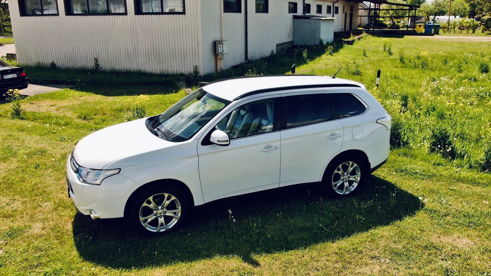 Balts apvidus auto stāv zāliena laukā pie mājas.