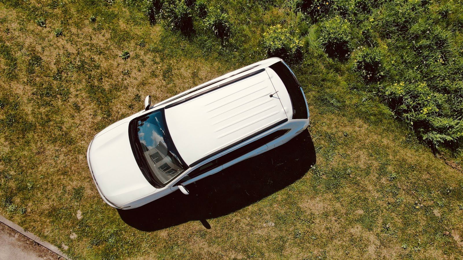 Skats no gaisa uz zālājā novietotu baltu automašīnu.