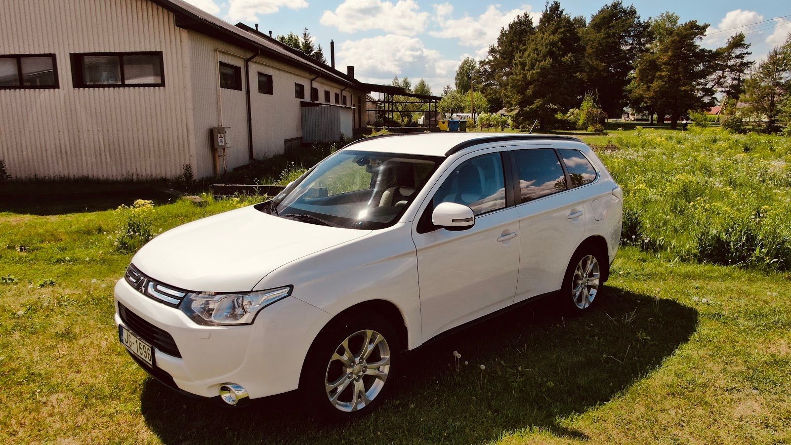 Balta automašīna ir novietota zāliena laukā pie ēkas.