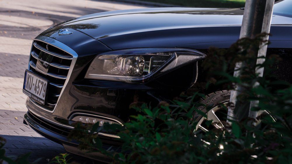 Stāvvietā pie koka stāv melna mašīna.