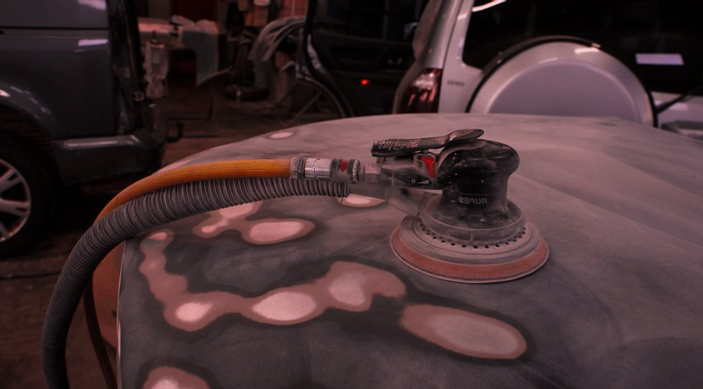 Tiek izmantota slīpmašīna uz automašīnas pārsega.