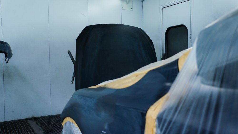 Cilvēks krāso auto krāsošanas kabīnē.