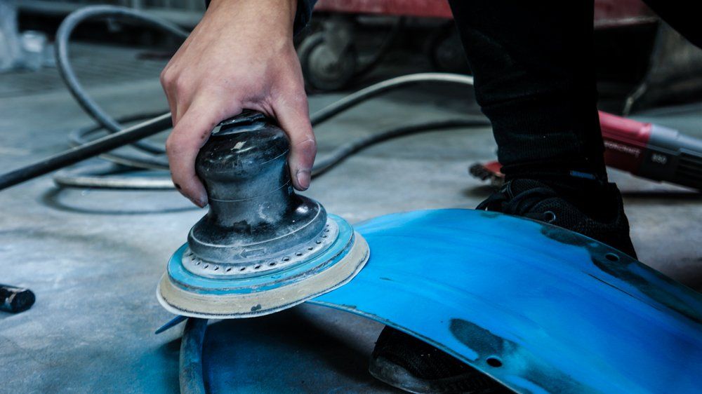 Cilvēks slīpē zilu priekšmetu ar slīpmašīnu.