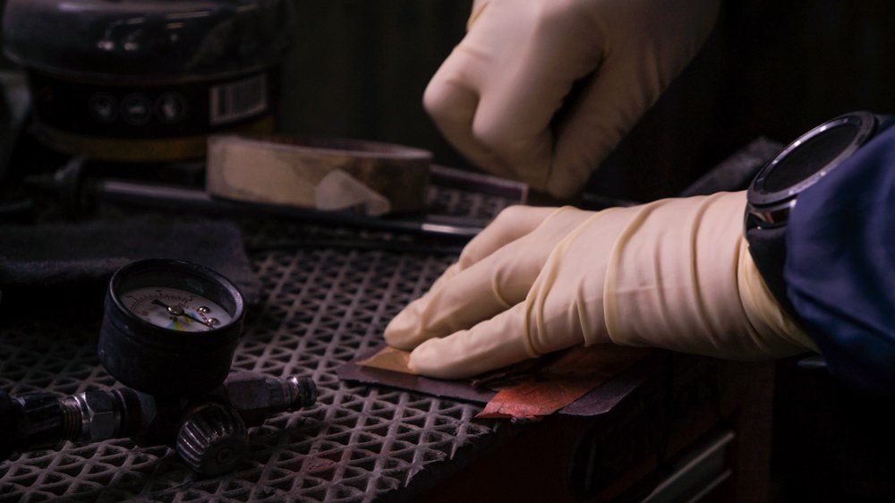 Cilvēks cimdos strādā pie metāla gabala.