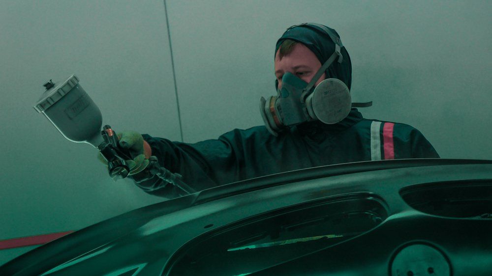 Vīrietis ar masku krāso automašīnu ar aerosolu.