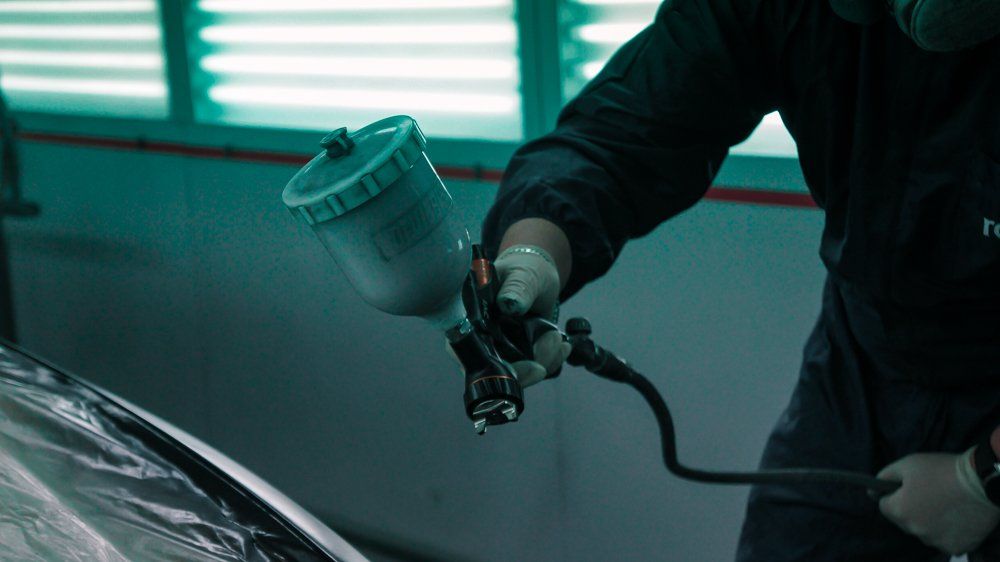 Vīrietis garāžā krāso mašīnu ar aerosolu.