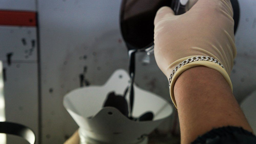 Cilvēks cimdos lej piltuvē šķidrumu