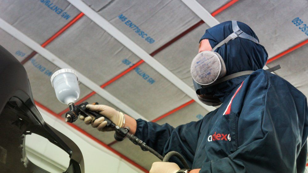 Vīrietis, kas valkā masku, krāso automašīnu ar aerosolu