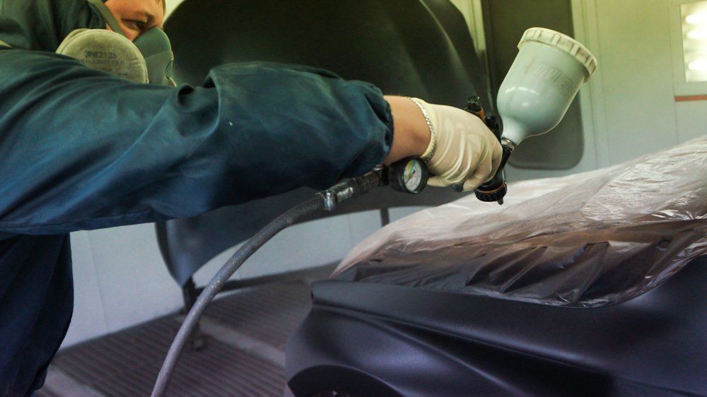 Vīrietis garāžā krāso mašīnu ar aerosolu.