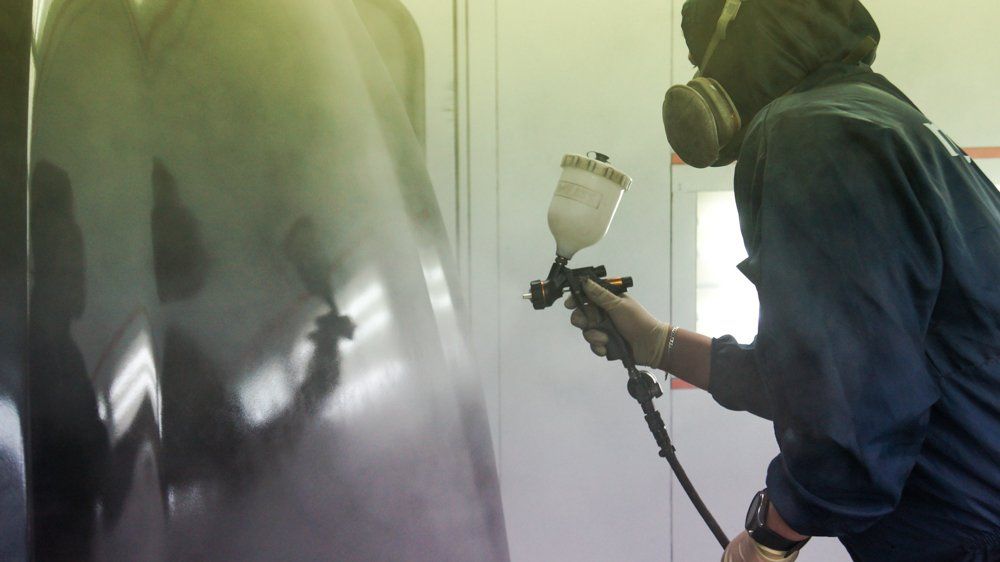 Vīrietis ar gāzmasku krāso sienu ar aerosolu.