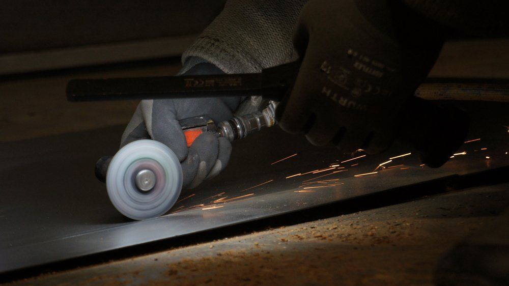 Cilvēks slīpē metāla gabalu ar dzirnaviņām.