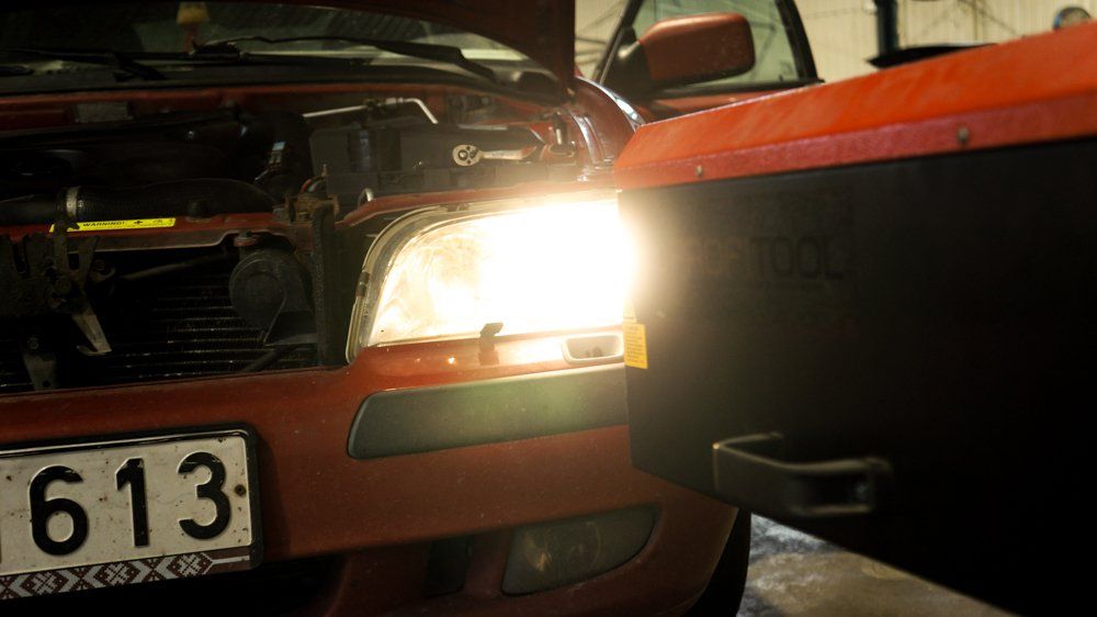 Sarkana mašīna ar atvērtu motora pārsegu stāv pie traktora.