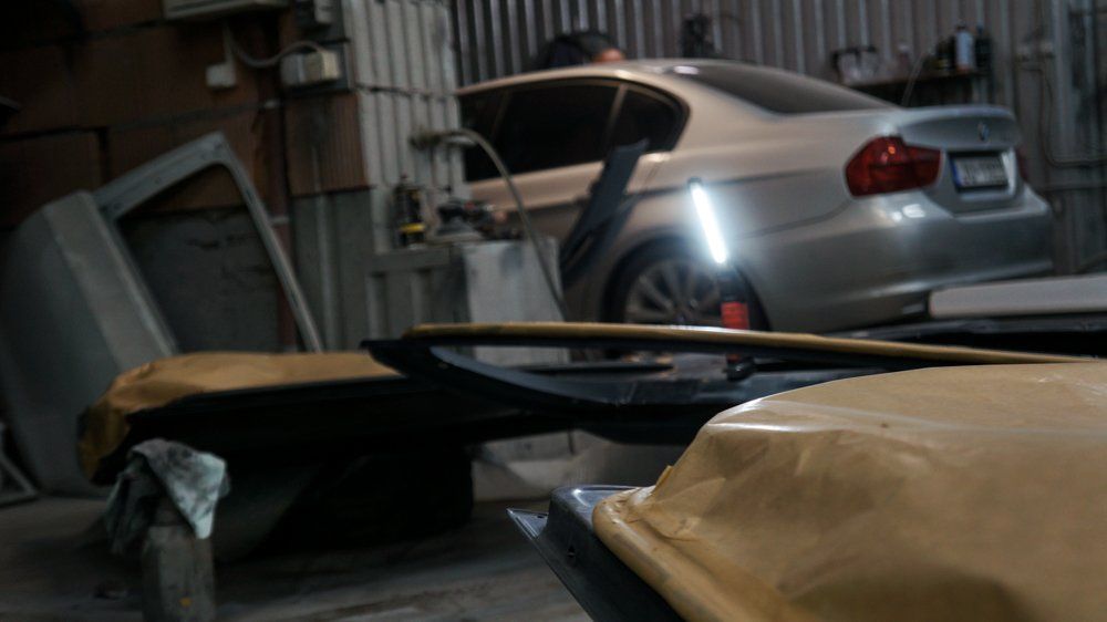 Sudraba auto stāv garāžā pie dzeltenas mašīnas.