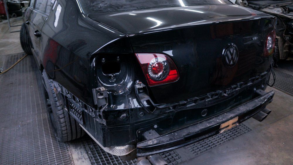 Melna mašīna ar bojātu aizmuguri sēž garāžā.