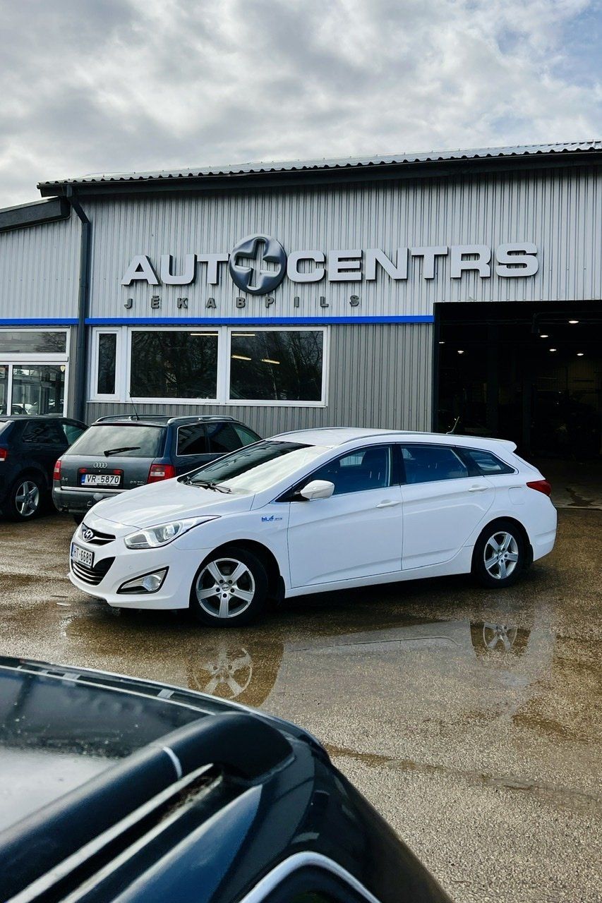 Balta automašīna ir novietota pie ēkas, uz kuras ir rakstīts auto centrs.