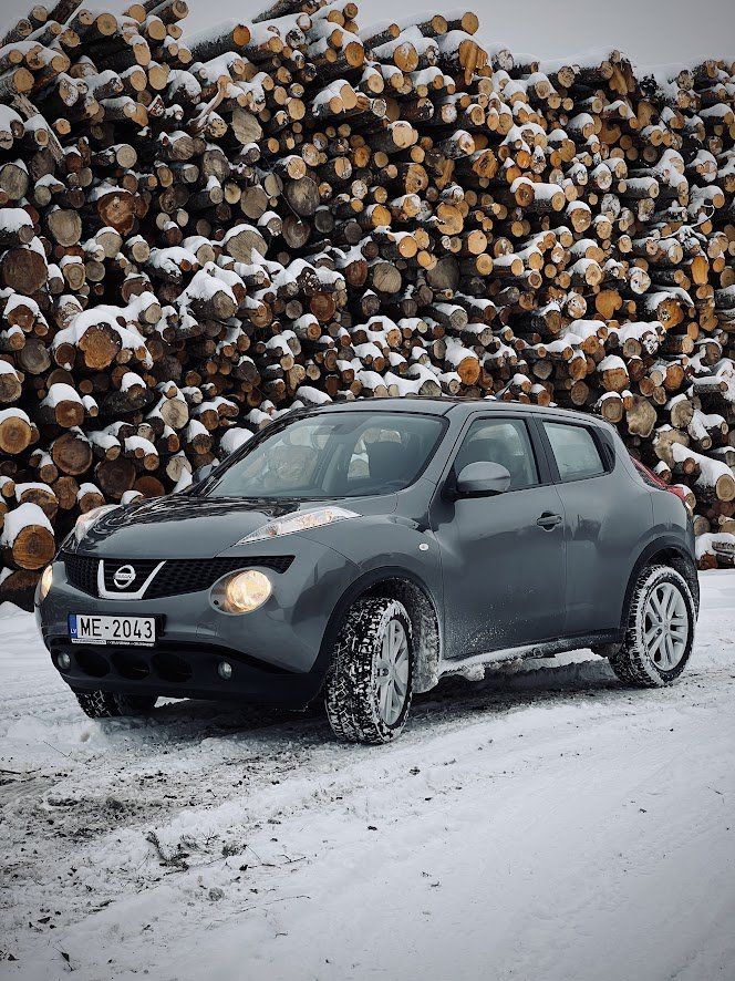 Automašīna stāv sniegā pie baļķu kaudzes.