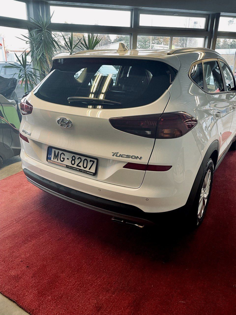 Balta automašīna ir novietota uz sarkanā paklāja salonā.