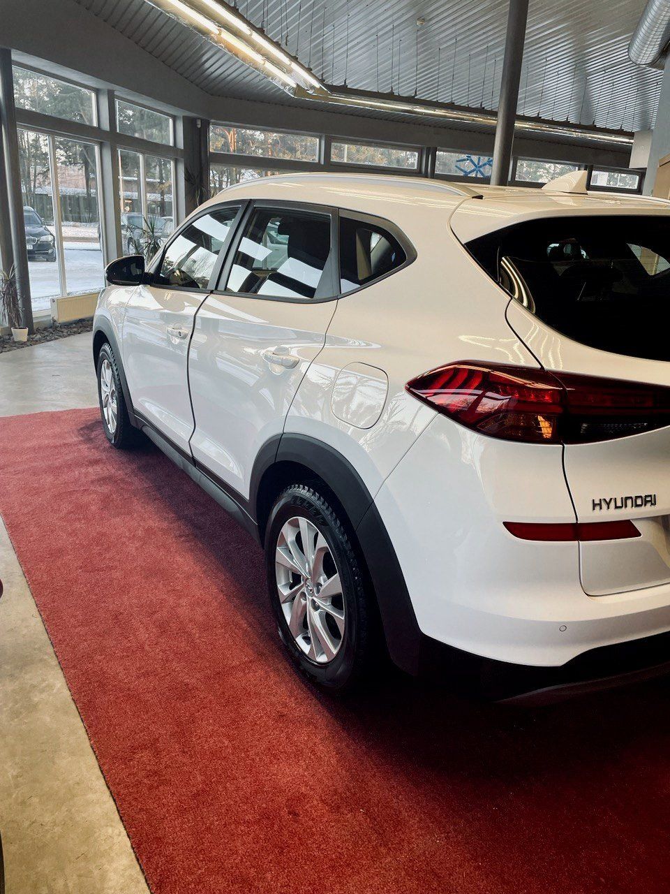 Balta mašīna ir novietota salonā uz sarkana paklāja.