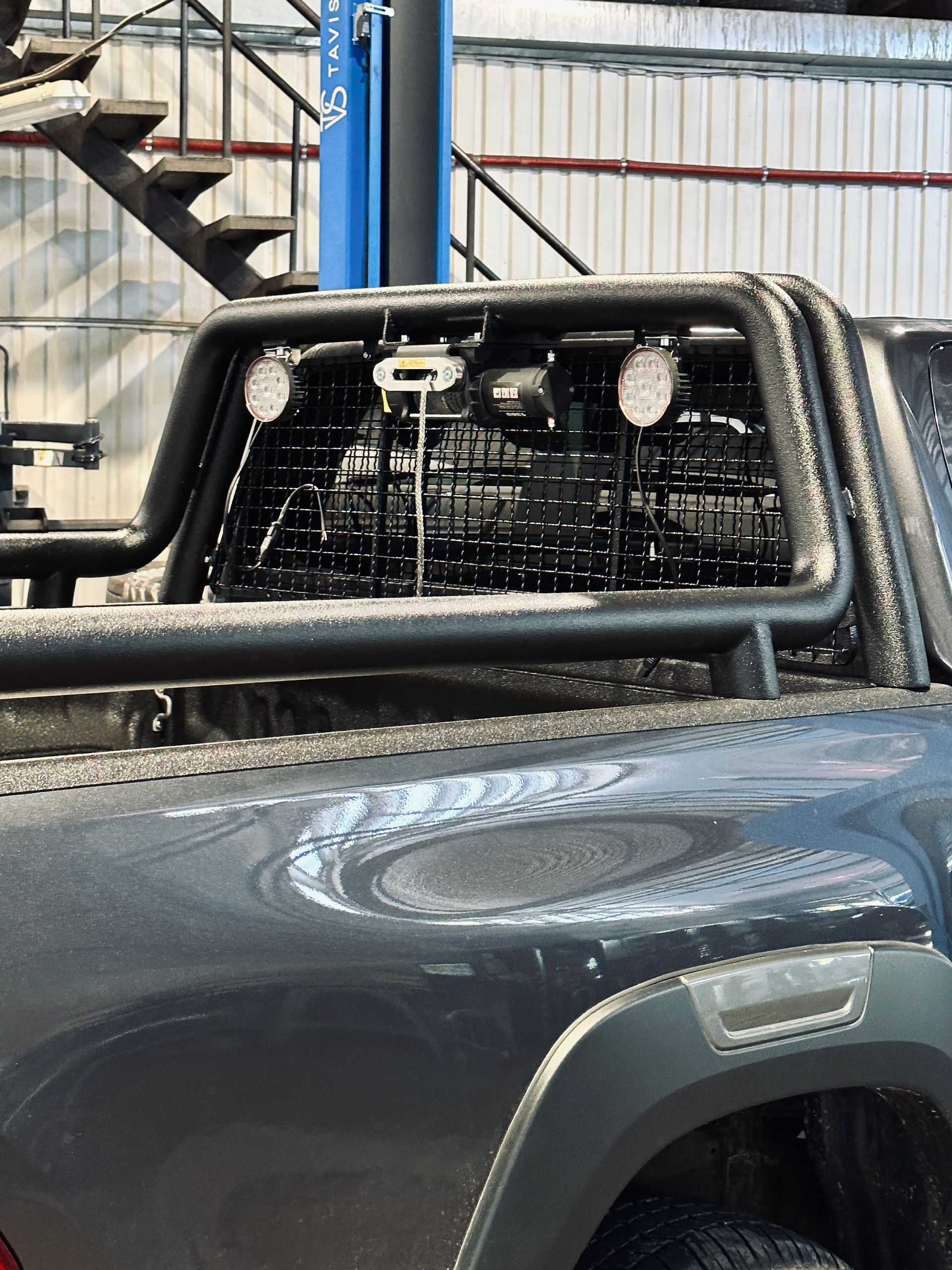 Garāžā stāv kravas automašīna ar būru aizmugurē.