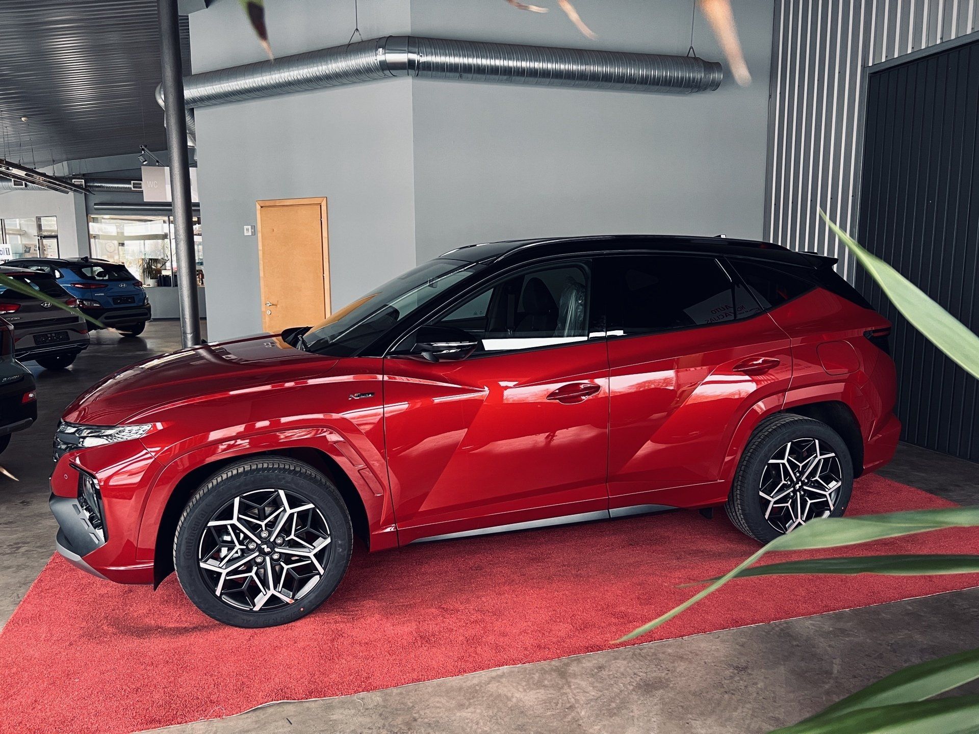 Sarkana automašīna ir novietota uz sarkanā paklāja izstāžu zālē.