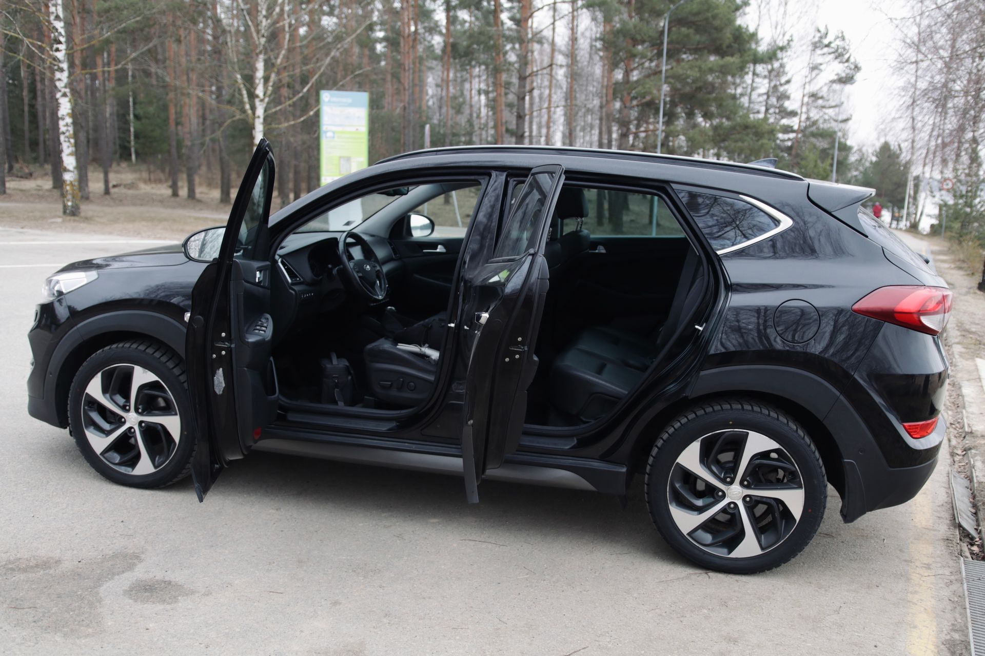 Ceļa malā stāv melns apvidus auto ar atvērtām durvīm.