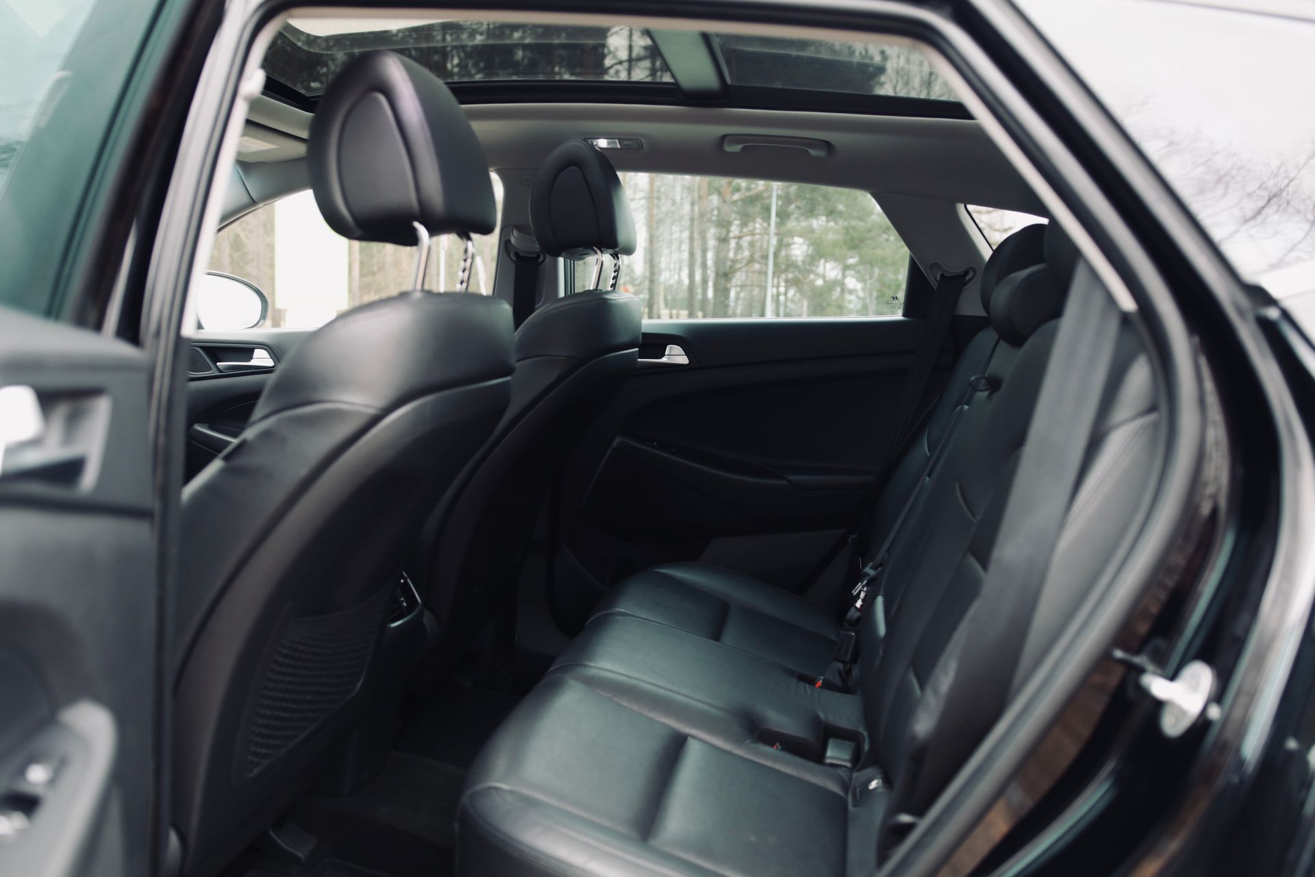 Melnas automašīnas aizmugurējais sēdeklis ar jumta lūku.