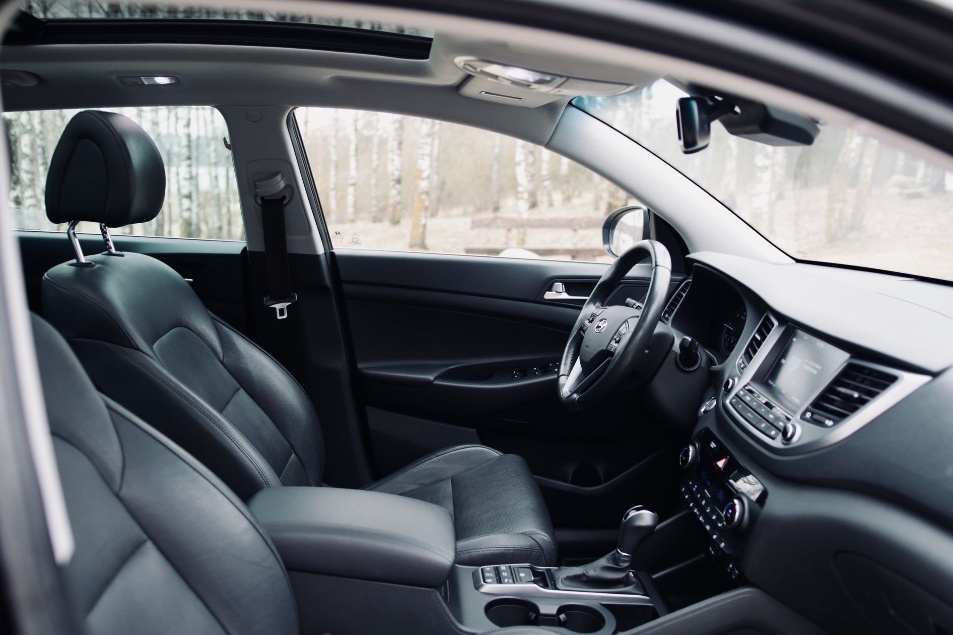 Melnas automašīnas salons ar ādas sēdekļiem un jumta lūku.