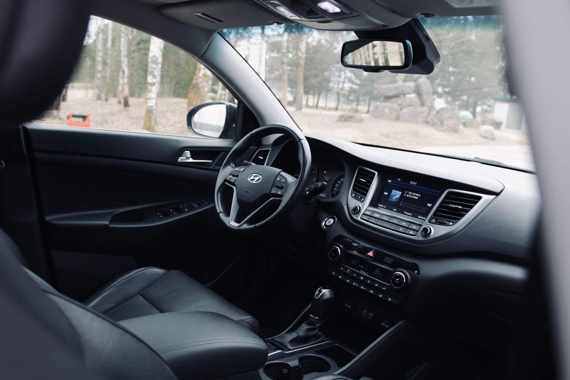 Melnas automašīnas salons ar stūri un instrumentu paneli.