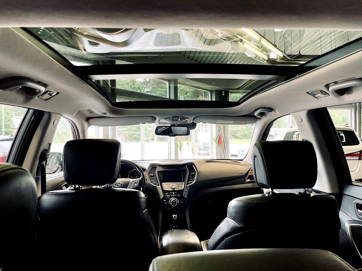 Automašīnas iekšpuse ar jumta lūku un melniem sēdekļiem.