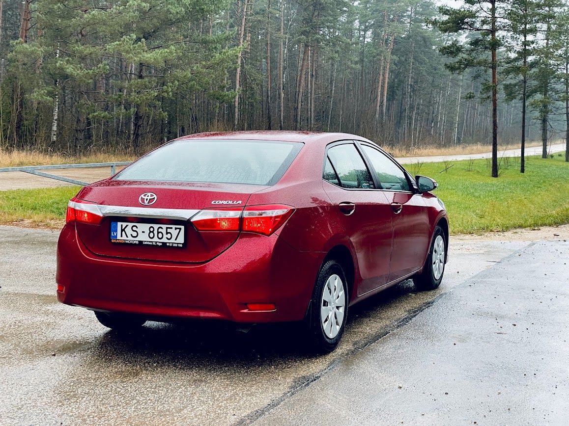 Lietū ceļa malā stāv sarkana mašīna.