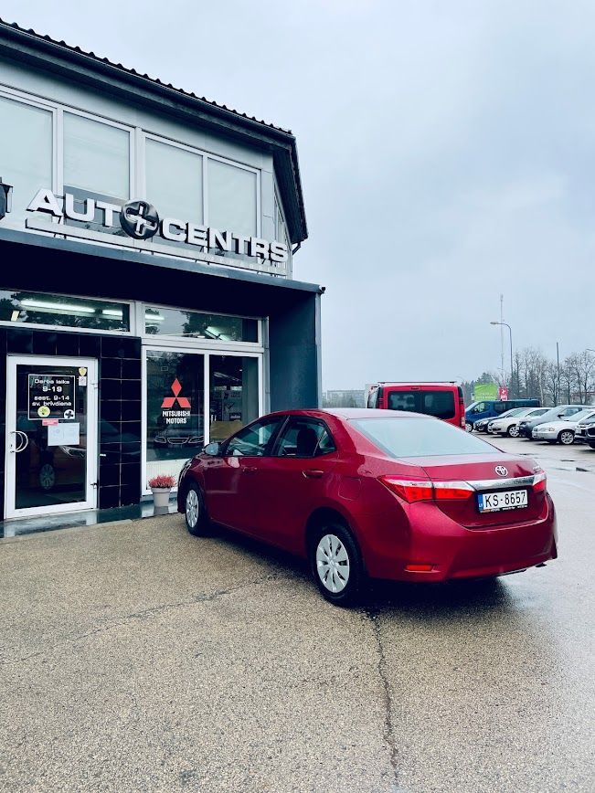 Sarkana automašīna ir novietota pie automašīnu tirdzniecības vietas.