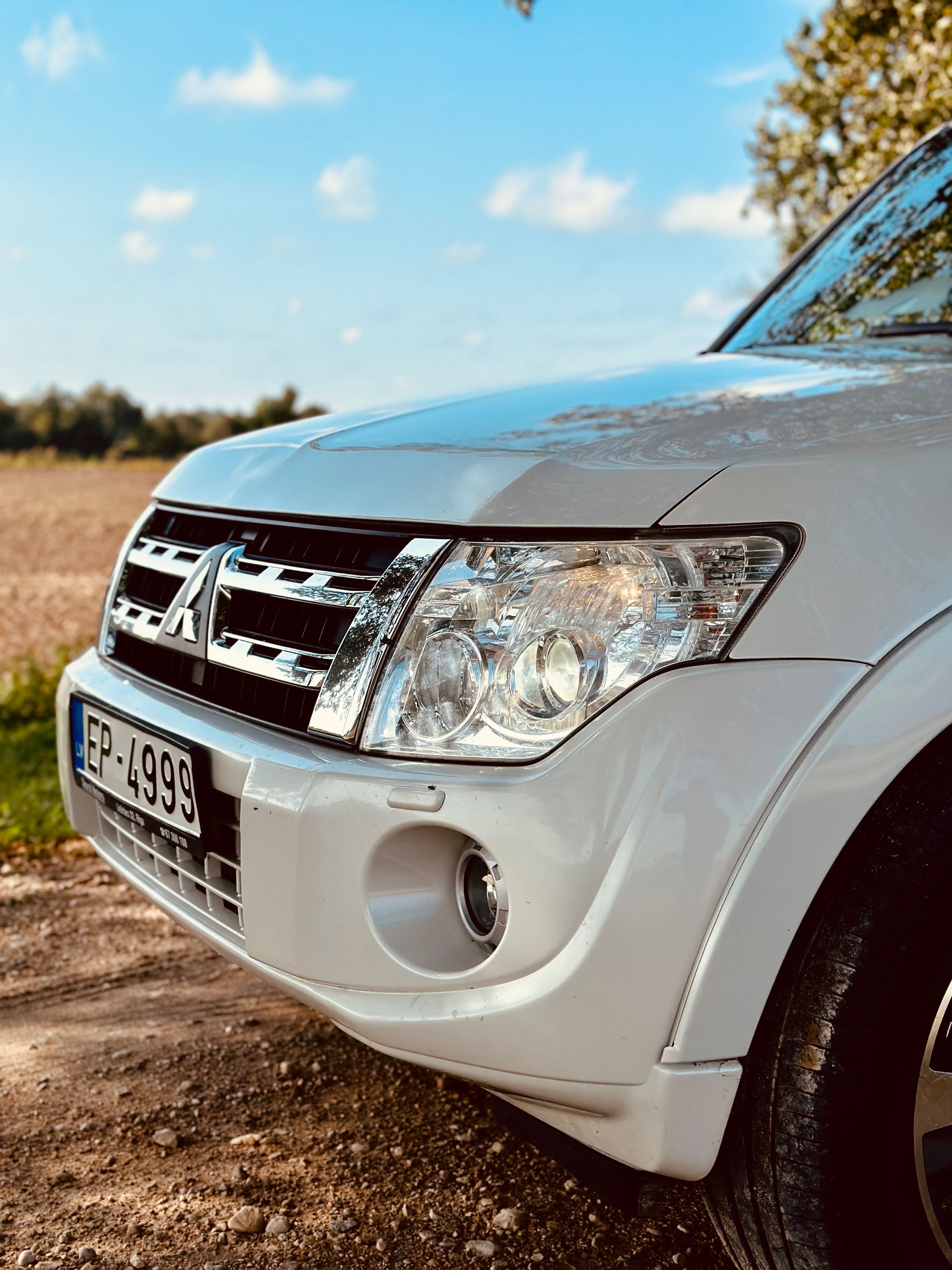 Zemes ceļa malā stāv balta mašīna.
