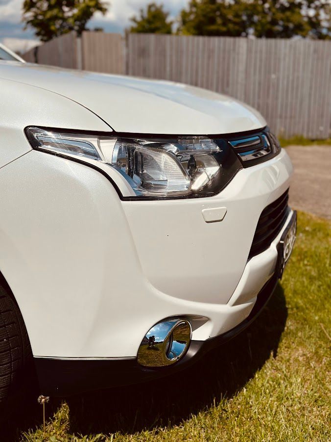 Balta mašīna stāv zālienā pie žoga.