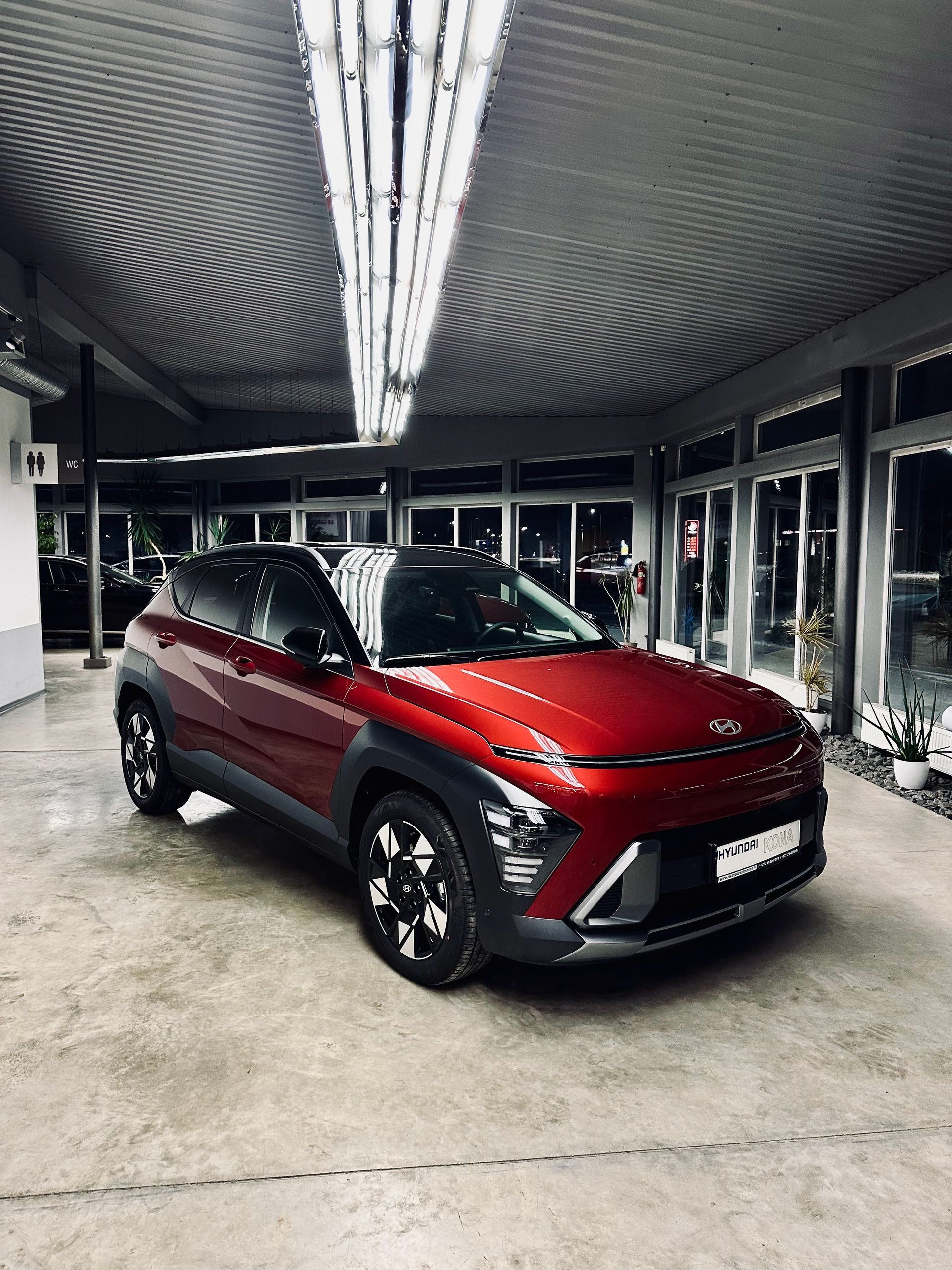 Sarkana automašīna ir novietota stāvvietā pie ēkas.