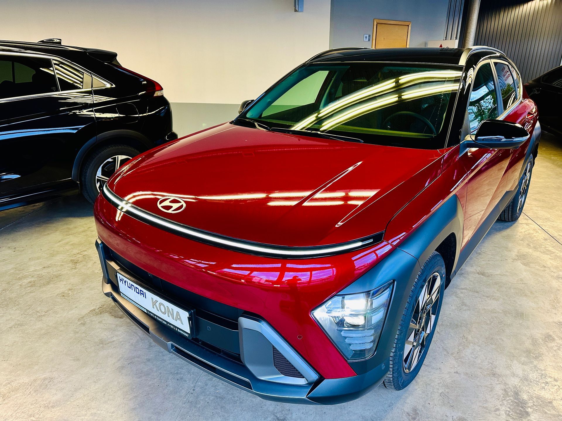 Sarkana mašīna stāv garāžā pie melnas mašīnas.